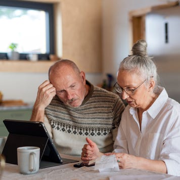 Senior couple sitting at the kitchen table looking at digital tablet and recalculating their expenses.