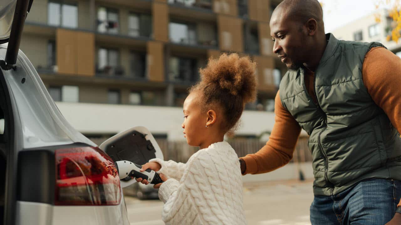 A Black father and his daughter plug in an electric vehicle.