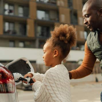A Black father and his daughter plug in an electric vehicle.