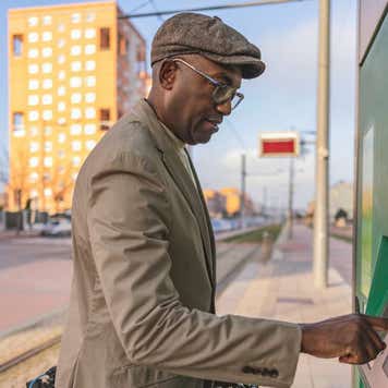Mature businessman with electric vehicle using ATM machine on footpath