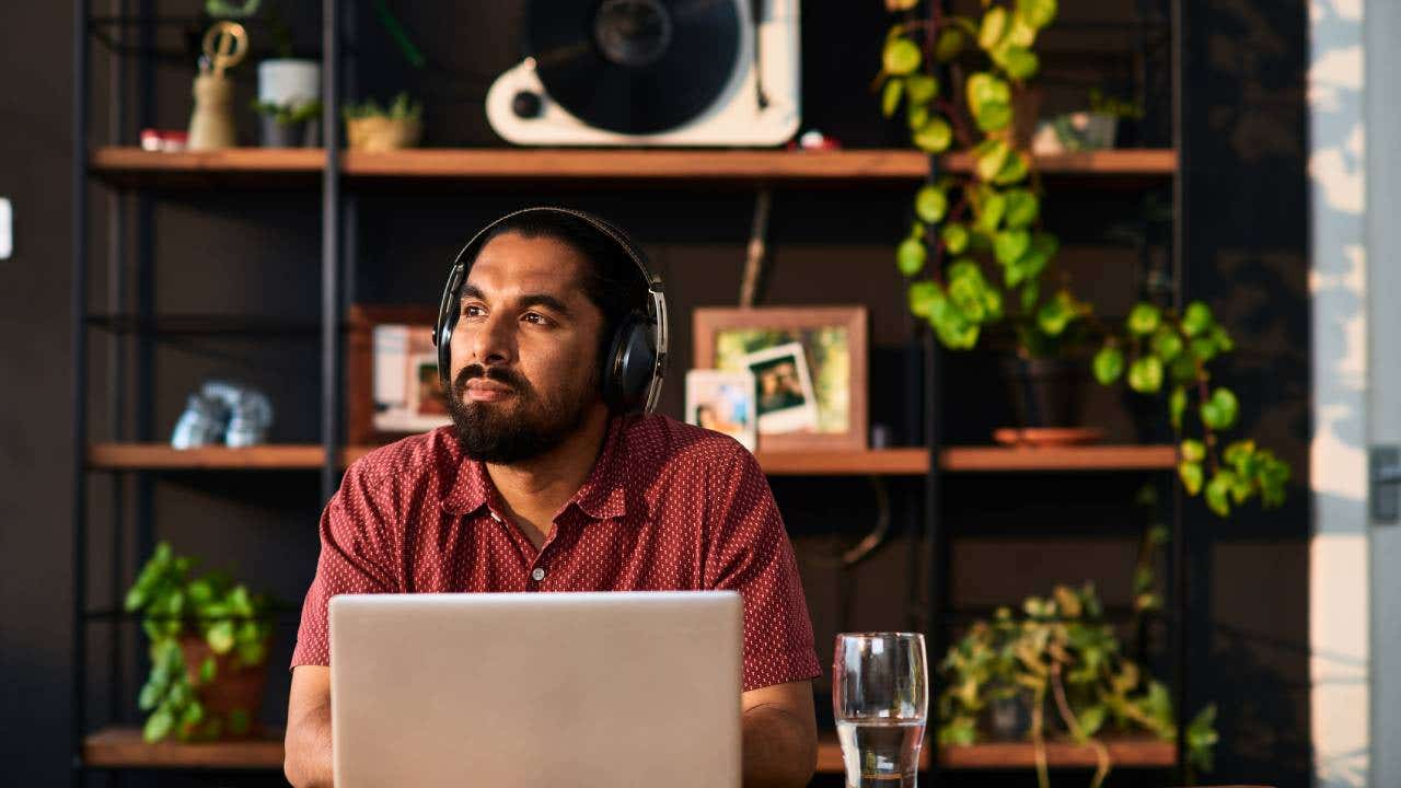 Mid adult man wearing headphones using laptop and looking away