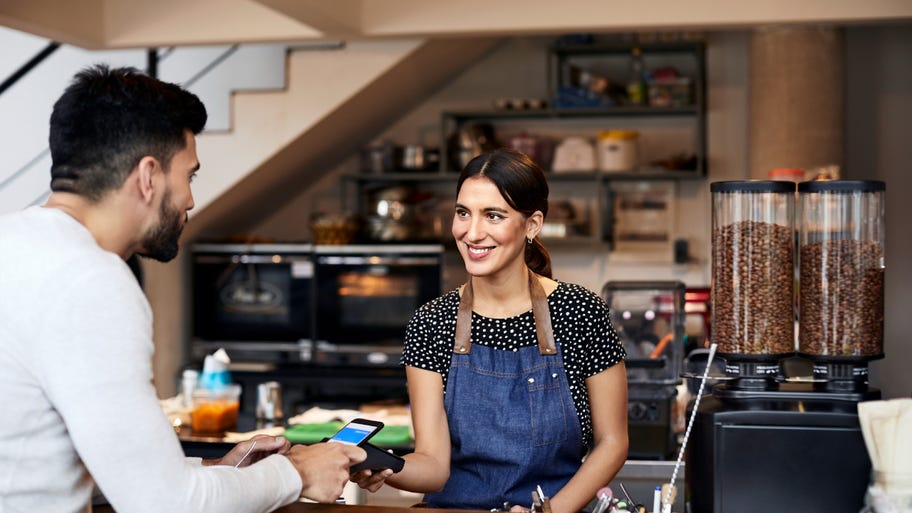 A coffeeshop owner works the front counter, accepting payment from a customer.