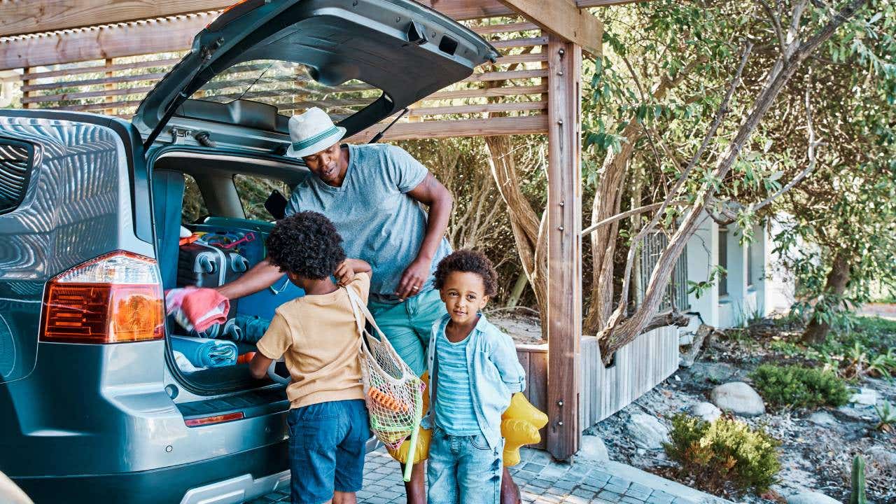 Father packing luggage in a car preparing to travel to the beach with his kids