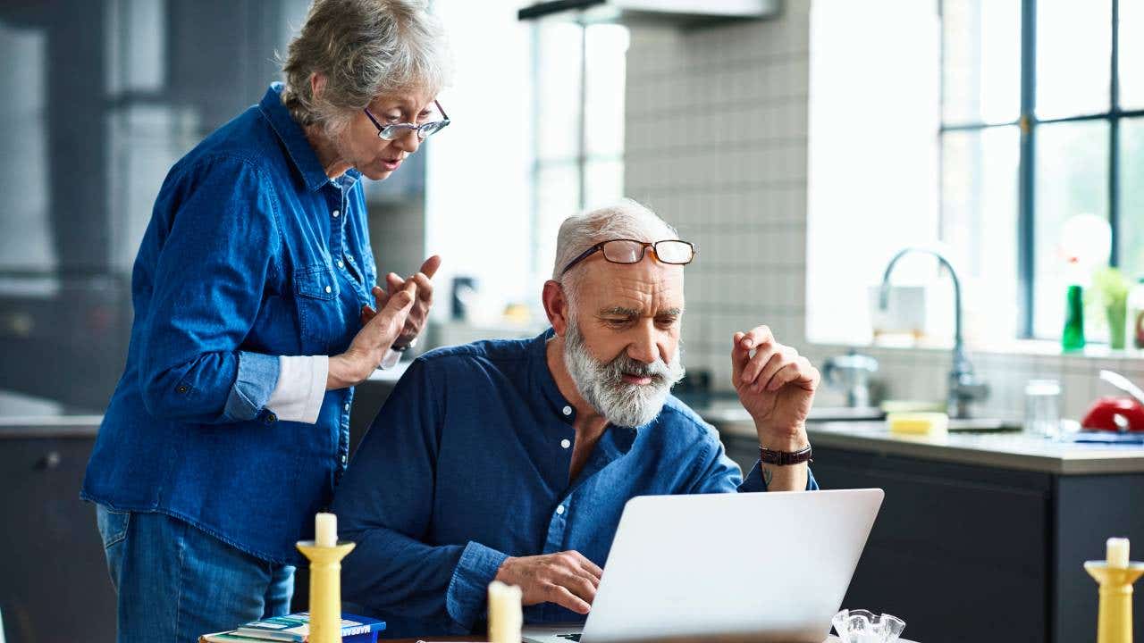 Senior man using laptop and woman watching over shoulder
