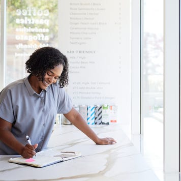 Female entrepreneur smiling while accounting on a checkout counter.
