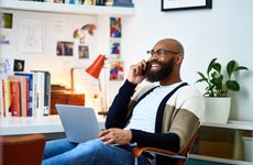 Man smiling and sitting with a laptop while on the phone.