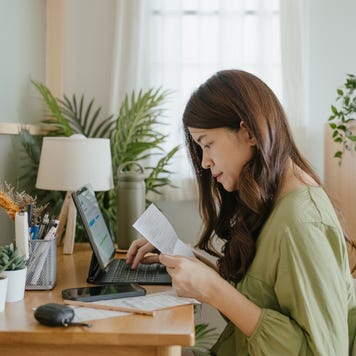 Woman holding paper various expense bills and plans for personal finances at her home.