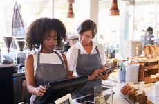 A business owner trains an employee on a new point of sale system.