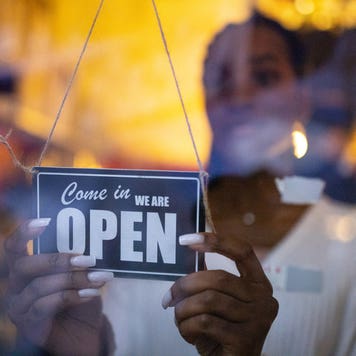 Woman turning an open sign on glass front door of coffee shop. Business owner hanging an open sign at a cafe.