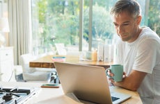 Man drinking coffee and working at laptop in kitchen
