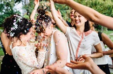 Newlywed lesbian couple dancing while friends and family throwing confetti on couple