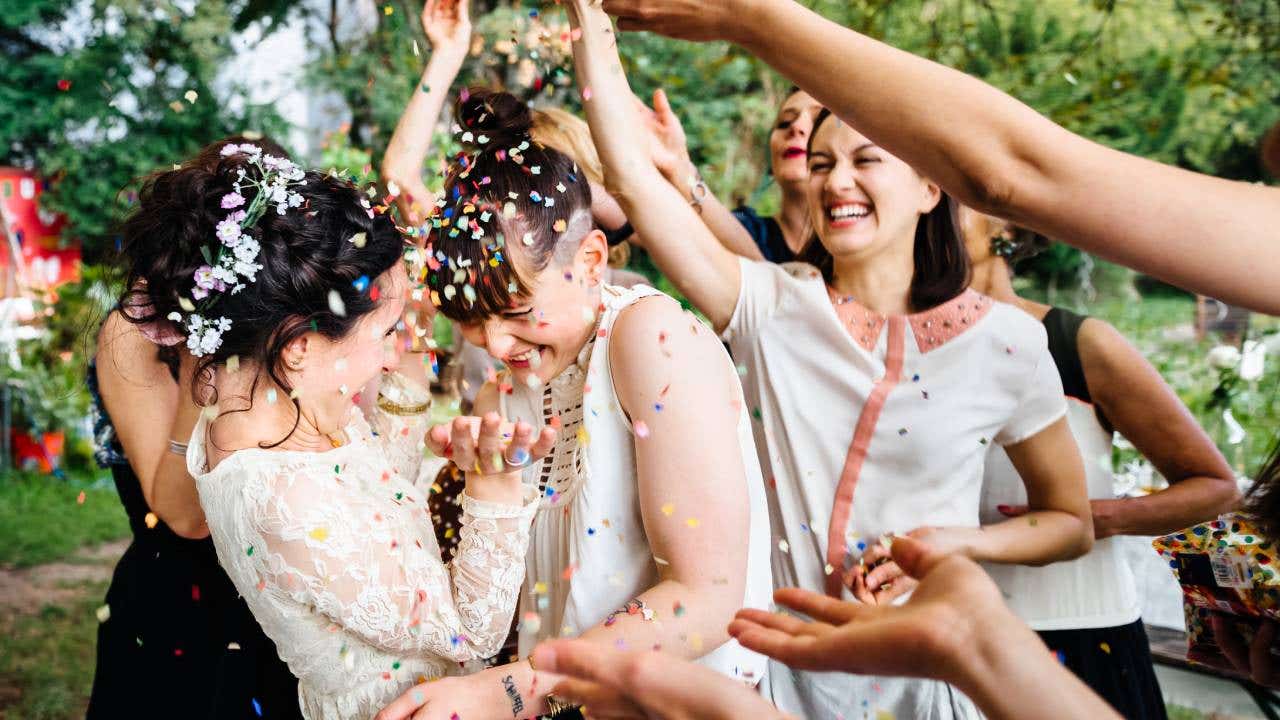 Newlywed lesbian couple dancing while friends and family throwing confetti on couple
