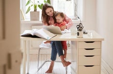 Woman sitting with daughter while working on laptop at home