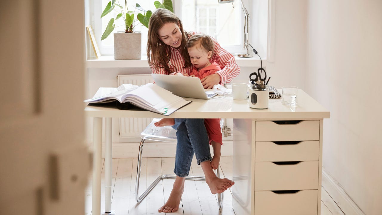 Woman sitting with daughter while working on laptop at home