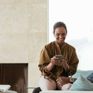 Smiling man looking at female partner with smart phone sitting on lap at home