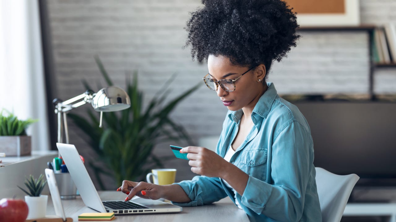 Pretty young afro woman shopping online with credit card with laptop while working on office at home.