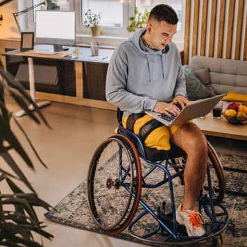 Man in wheelchair typing on laptop indoors