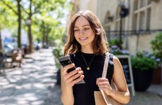 Smiling young woman with smartphone walking on the street