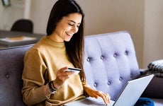 Young woman with credit card shopping over laptop while sitting at home