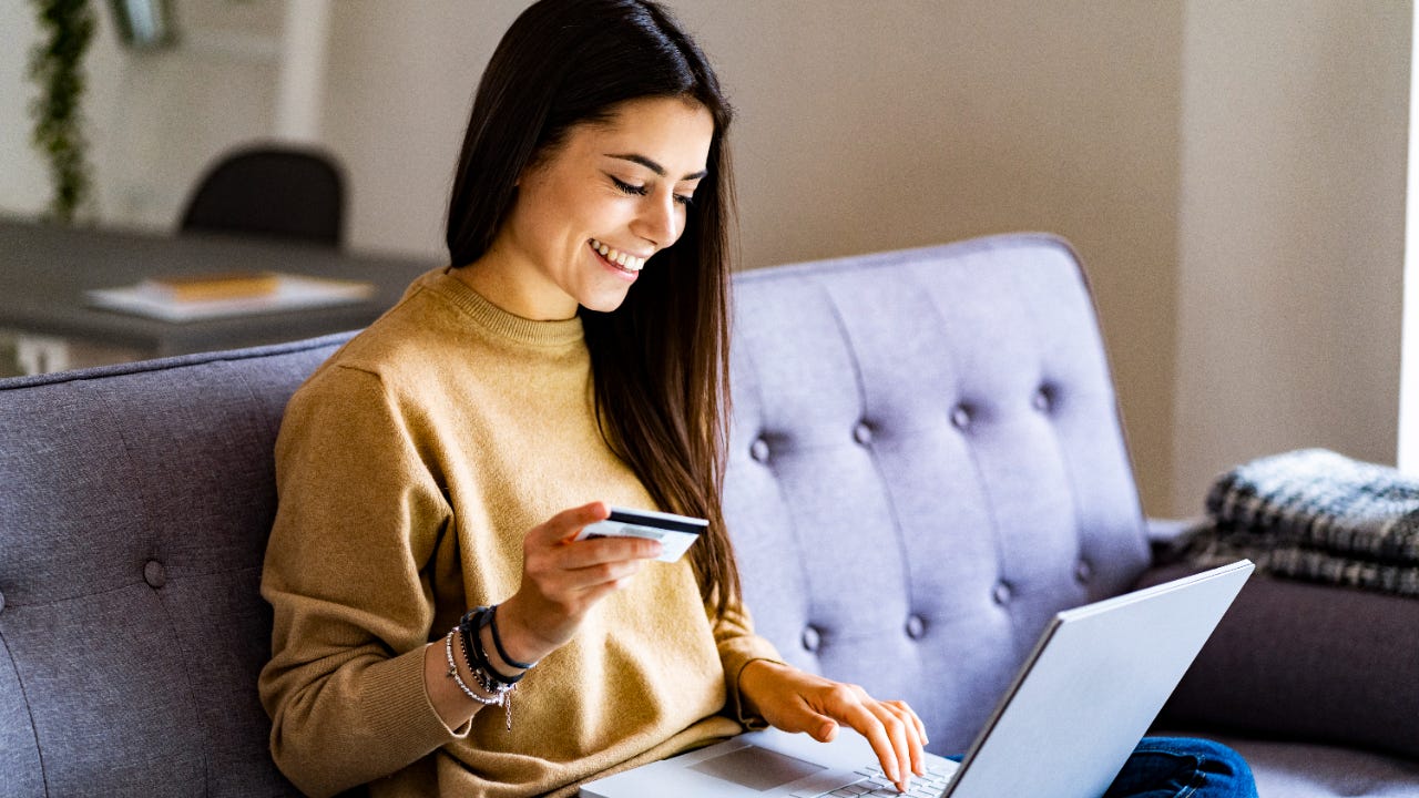 Young woman with credit card shopping over laptop while sitting at home