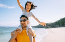 Father carrying young daughter on shoulders on beach