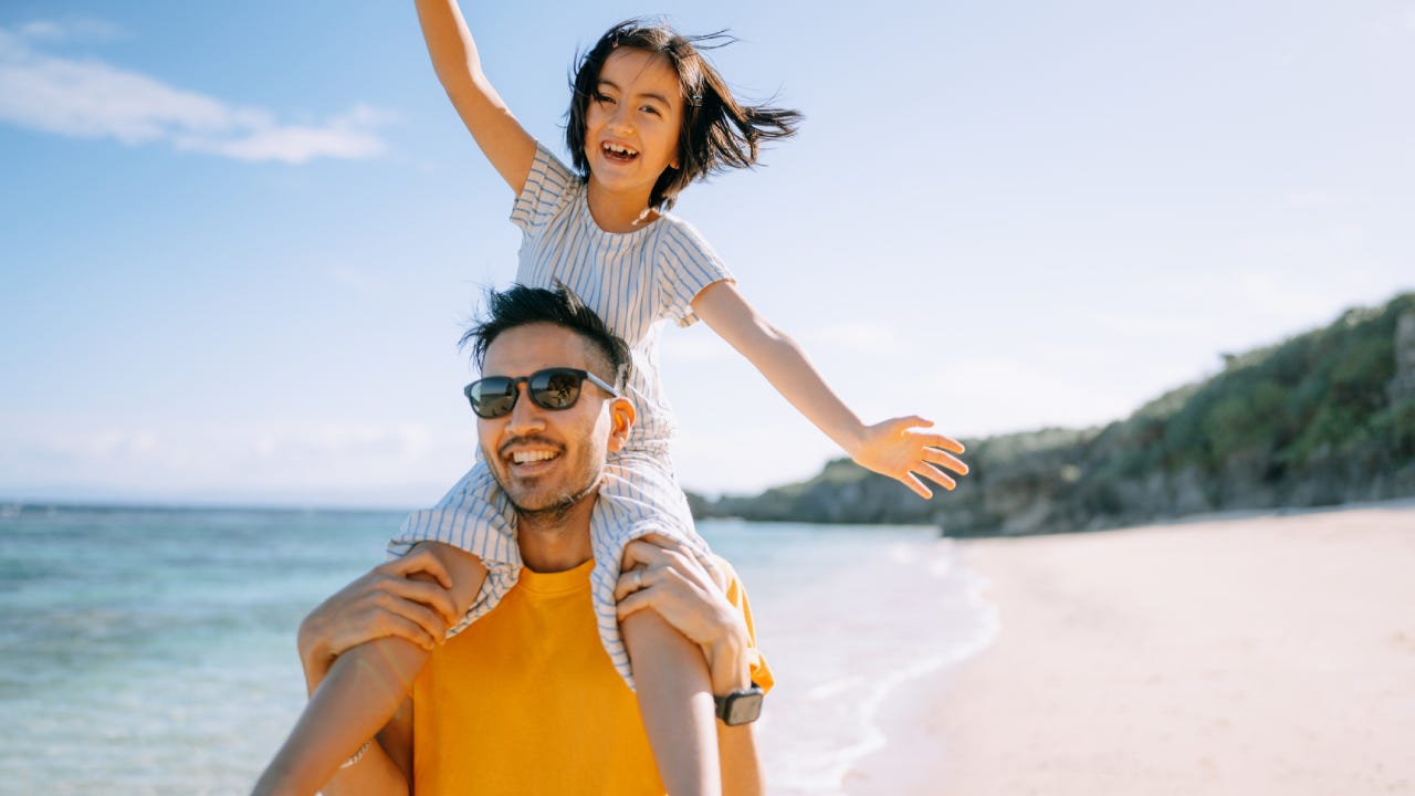 Father carrying young daughter on shoulders on beach