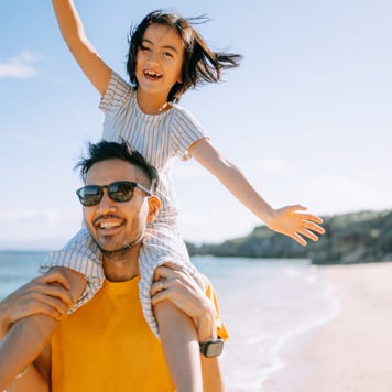 Father carrying young daughter on shoulders on beach