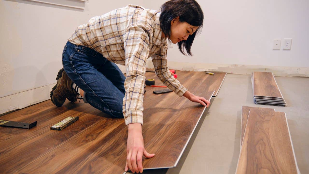 A woman installing laminate flooring in her home.