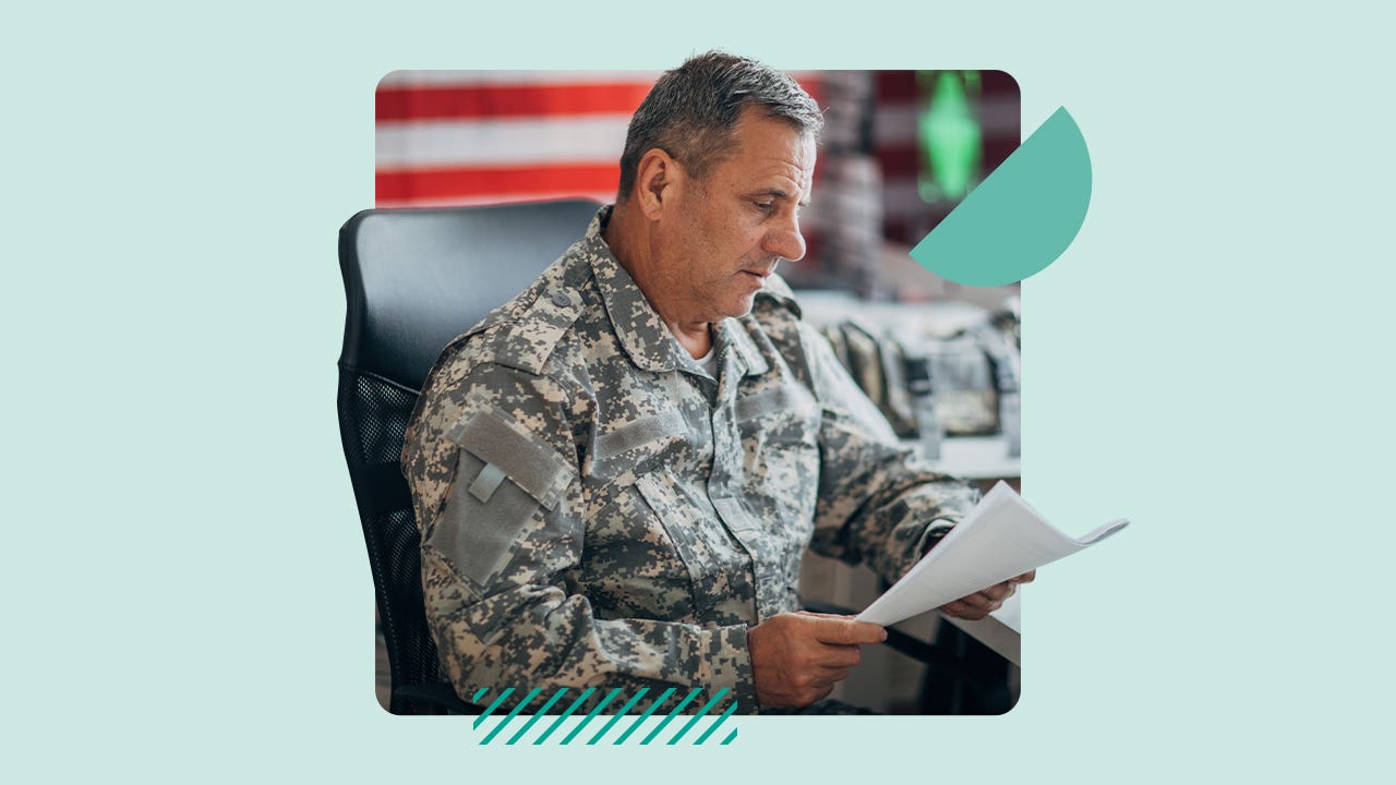 A man wearing army fatigues looks over paperwork in his office.