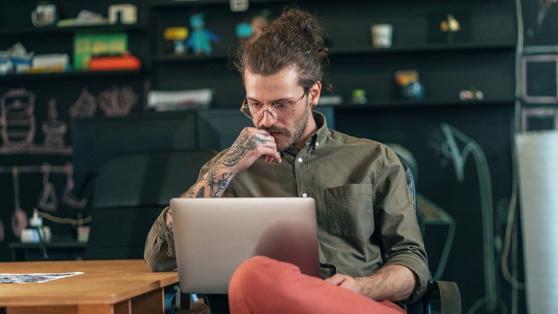 Young man with tattoos studying something on a laptop in a cafe