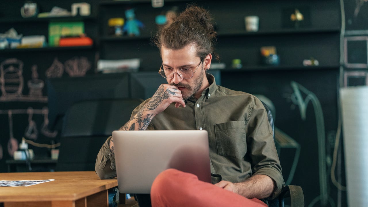 Young man with tattoos studying something on a laptop in a cafe