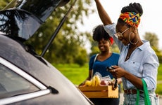 Candid shot of young Black woman opening trunk on her car to load a reusable shopping bag and a crate with groceries with a help of her friend.