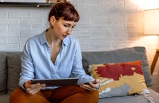A woman sitting on a sofa and using a tablet at her home for online shopping.