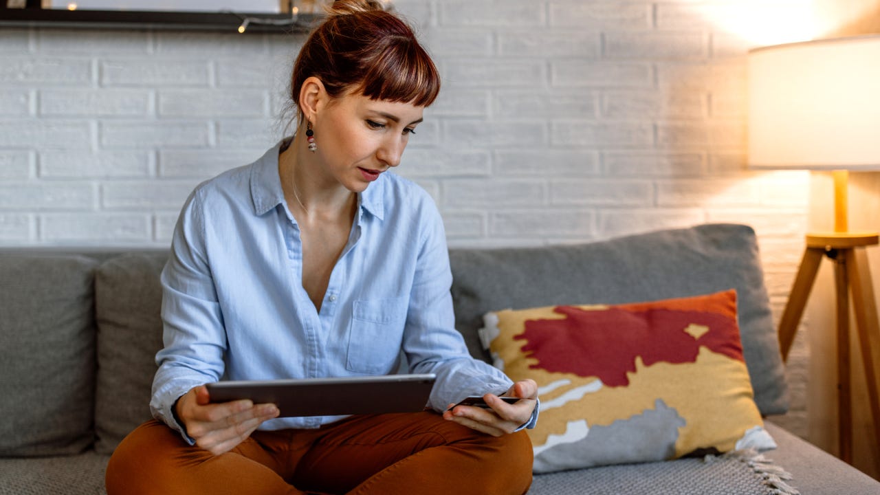 A woman sitting on a sofa and using a tablet at her home for online shopping.