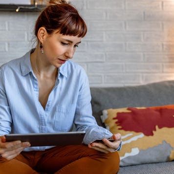 A woman sitting on a sofa and using a tablet at her home for online shopping.