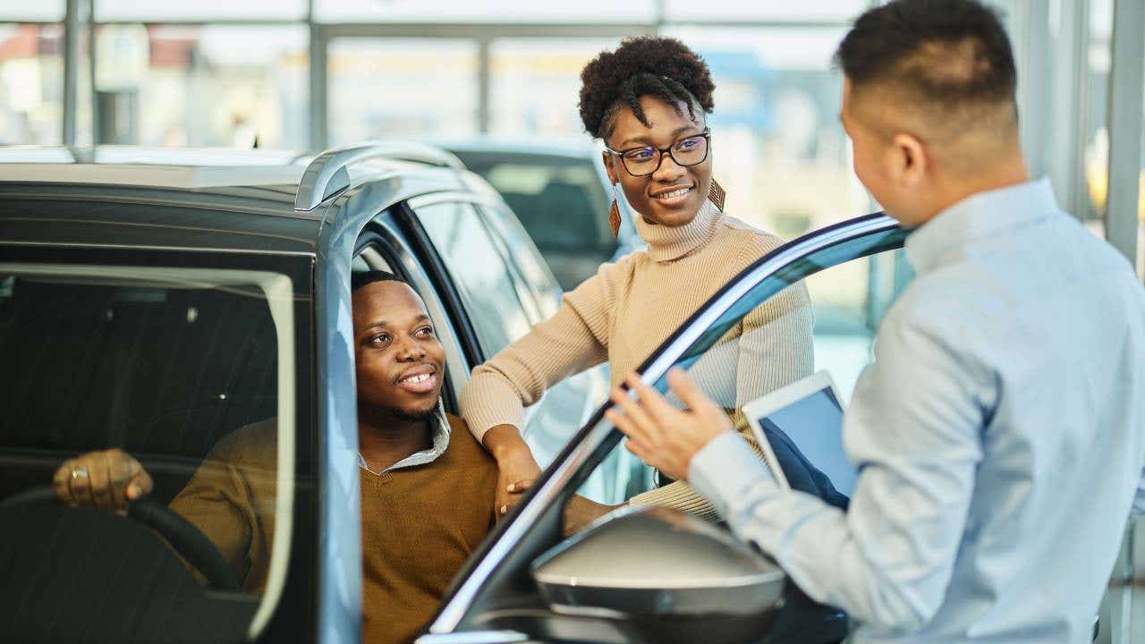 Happy black couple talking to car salesperson in a showroom