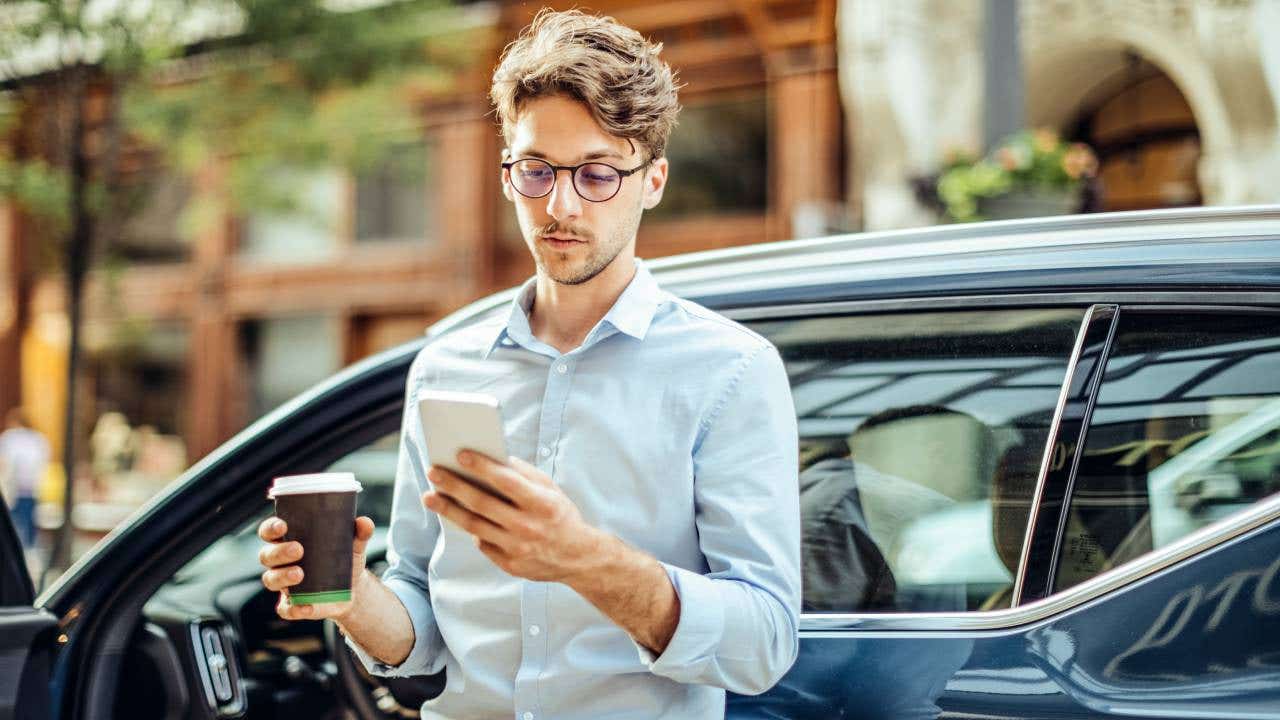 Young white man checking his phone outside of his car.