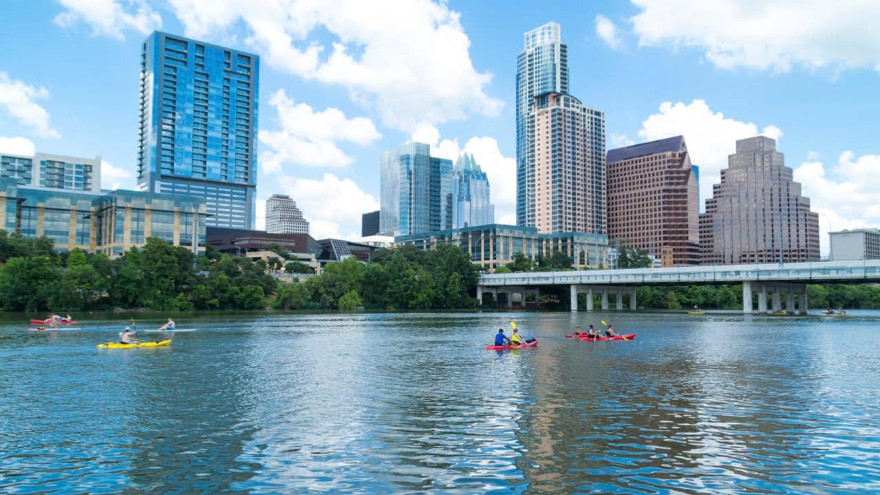 A distant view of people canoeing on Lady Bird Lake in Austin Texas with the Austin skyline in the background