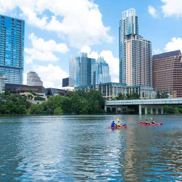 A distant view of people canoeing on Lady Bird Lake in Austin Texas with the Austin skyline in the background