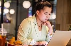 Businesswoman working at laptop with fast food on restaurant table