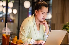 Businesswoman working at laptop with fast food on restaurant table