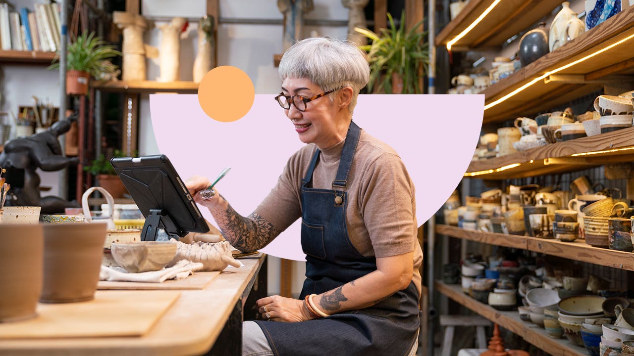 Older woman with tattoos works on a tablet in a ceramic studio.