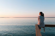 Young woman sitting on edge looks out at view of sunset and sea behind in Michigan