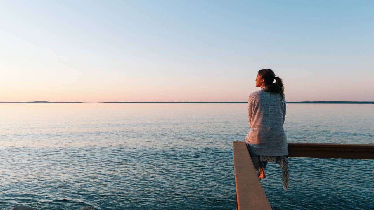 Young woman sitting on edge looks out at view of sunset and sea behind in Michigan