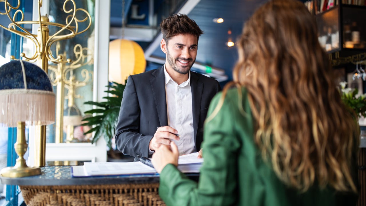 Male hotel receptionist helping a woman guest in checking in process. Woman in hotel check-in at reception talking with the concierge at front office.