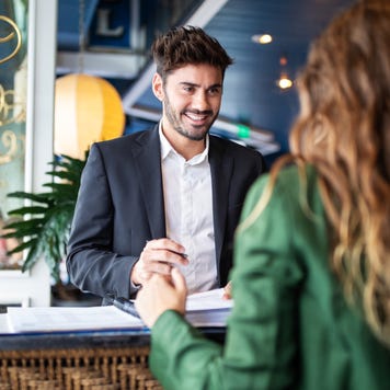 Male hotel receptionist helping a woman guest in checking in process. Woman in hotel check-in at reception talking with the concierge at front office.