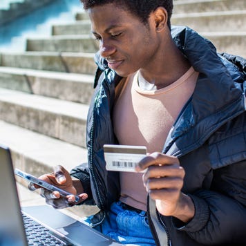 Gay guy sitting using laptop paying online with credit card, Lifestyle of gay guy on stairs using laptop, cell phone and credit card