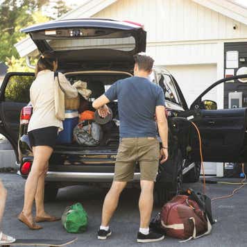 Portrait of mother, father and two daughters standing by car at electric vehicle charging station