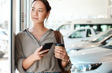 Shot of a young woman using her smartphone in a car dealership