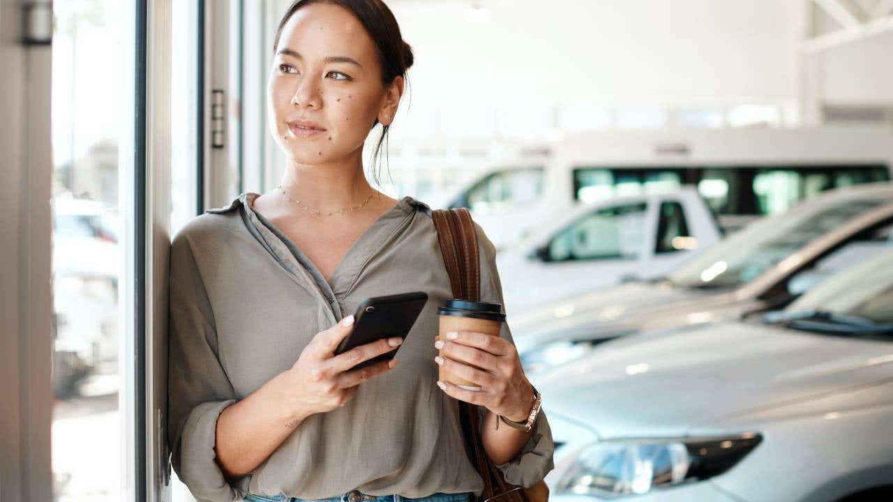 Shot of a young woman using her smartphone in a car dealership